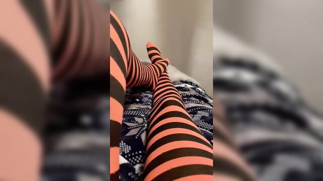 Closeup of sexy legs in orange black striped tights on bed, teasing body play