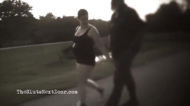Curvy brunette in tight black dress walks hand-in-hand with man in park at dusk