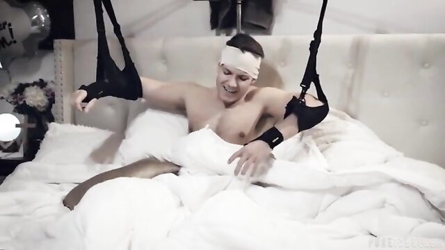 Blindfolded muscular guy bound in sex swing pleasures himself