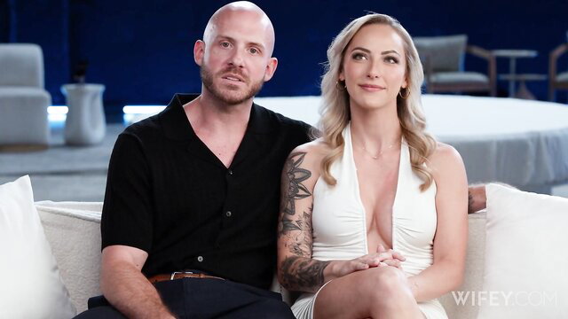 Hot blonde wife in white dress sits with tattooed bald husband watching BBC action