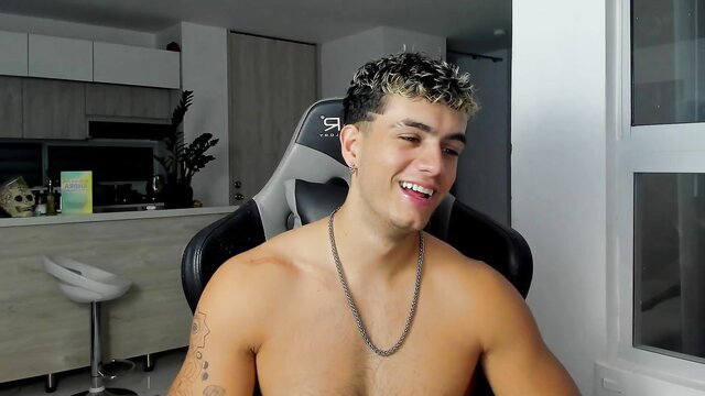 Shirtless Latino twink Noha Miler smiling topless in gamer chair