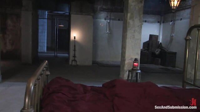 Holly Heart in dark dungeon bed, bound submission scene