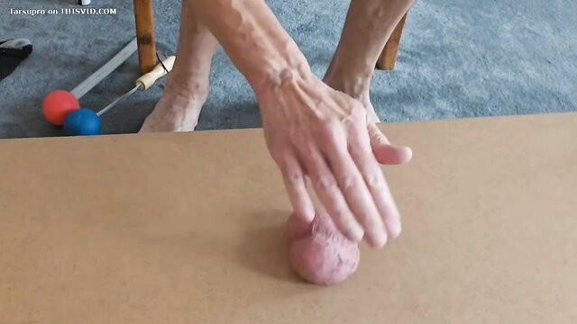 Elderly man groping large pink testicle balls on table