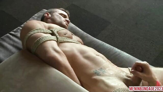 Bound man lying on a mattress, rope around his torso and arm