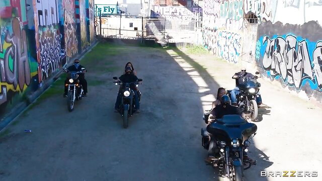 Kira Noir and Ryan Reid with black bikers on motorcycles in urban alley