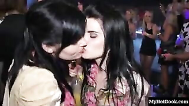 Two women kissing in front of a crowd of strippers