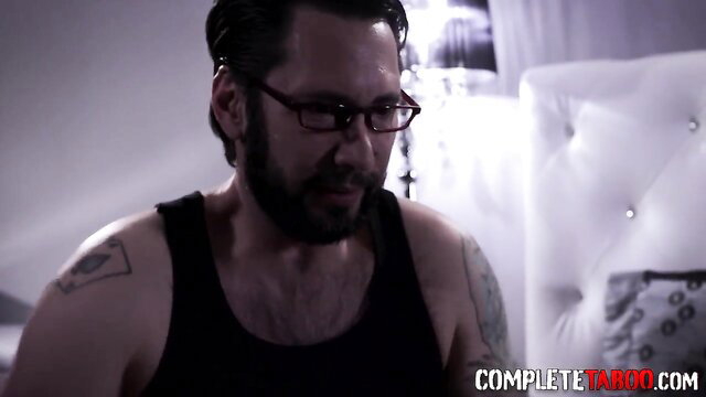 Tommy Pistol in tank top with tattoos on luxurious bed