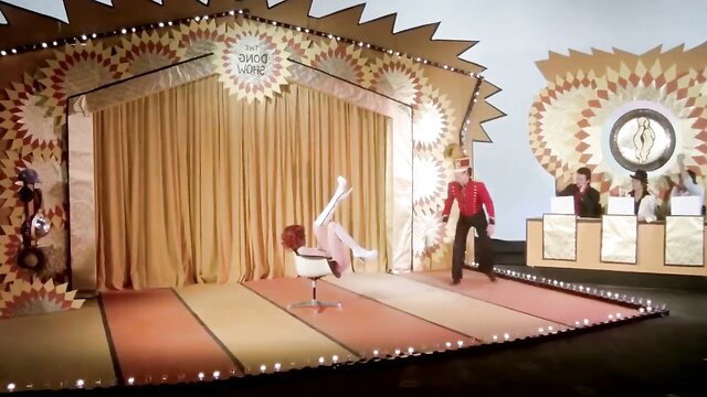 Carol Connors nude on game show stage with red-suited host