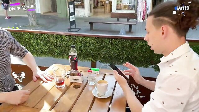 Two men at cafe table chatting, drinks and phone