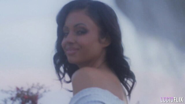 Daisy Fuentes smiling on rooftop in off-shoulder dress, soft lighting