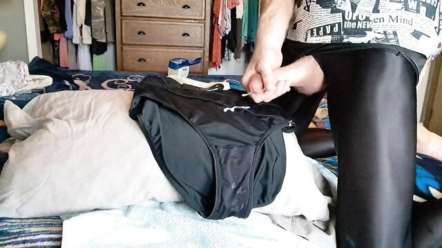 Trans in shiny black leggings stuffing black Puma panties on bed