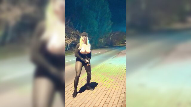 Blonde transvestite in tight black bodysuit strips outdoors at night