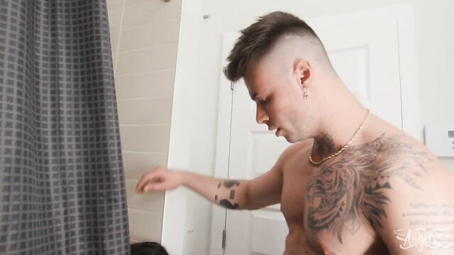 Tattooed muscular guy nude in shower, hand near cock in steamy bathroom