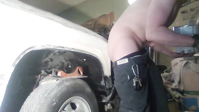 Shirtless muscular guy in low jeans working on white truck wheel