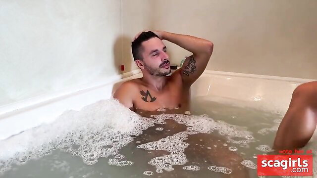 Tattooed stud in bubbly bath with blond babe's leg, raunchy wet fun