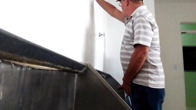 Mature man in striped shirt standing by metal toilet tank in bathroom