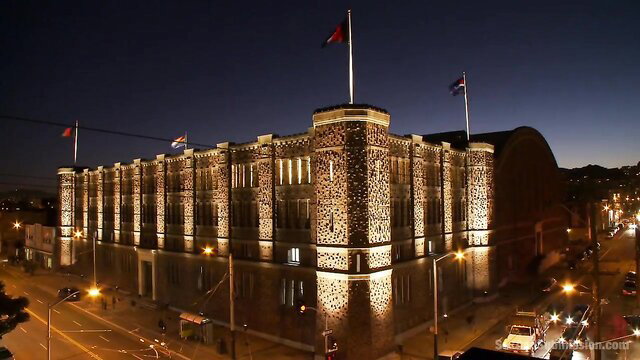 Lit historic prison building at night with flags, BDSM punishment vibe