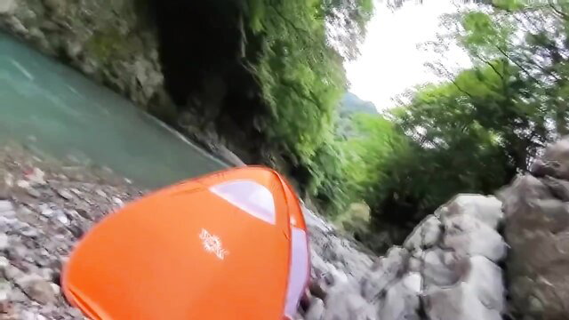 Orange tent by turquoise river in lush green gorge, outdoor adventure