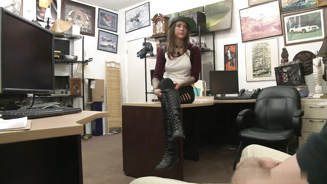 Tattooed brunette in beret and thigh-high boots sits on desk in office