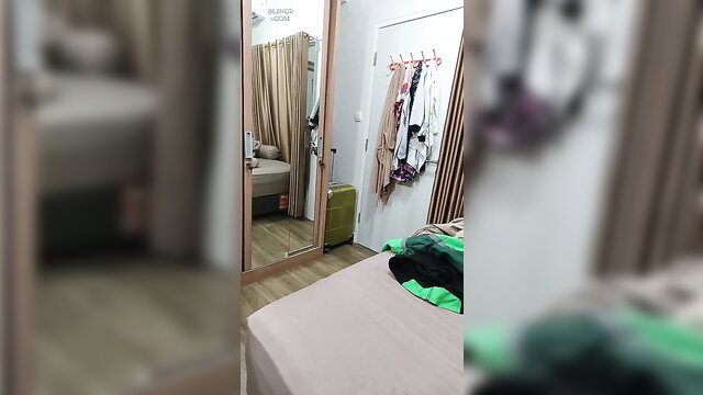 Indonesian amateur bedroom with clothes on bed and rack, mirror view