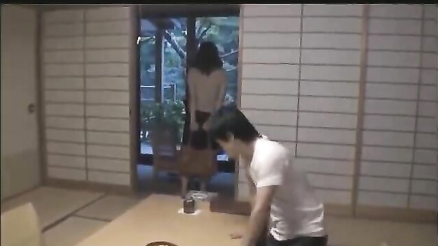 Japanese mom in skirt stands over son kneeling on floor at home