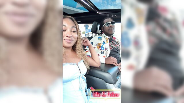 Mixed black couple in car, smiling girl with curly hair leans on shades guy