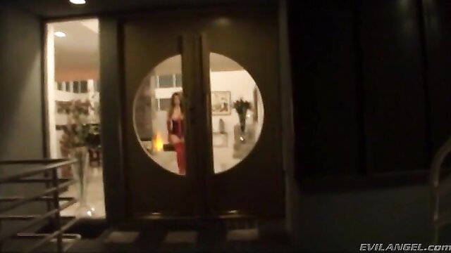 Brunette in red dress at round window door, Evil Angel adult scene