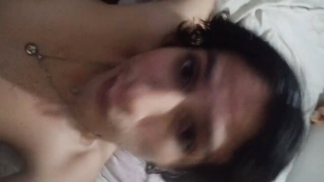 Blurry selfie of topless femboy lying in bed, necklace visible