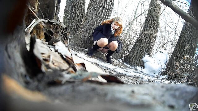 Ginger bridesmaid squats peeing behind tree in snowy forest