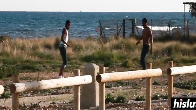 Two athletic black guys balancing on logs by beach in tight jeans