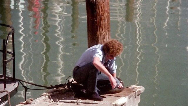 Vintage 1976 porn star with curly red hair crouching by water dock