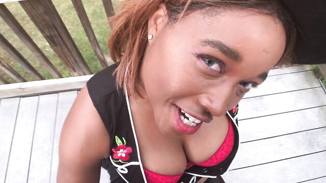 Hot black cowgirl in black vest and red bra smiles on backyard deck