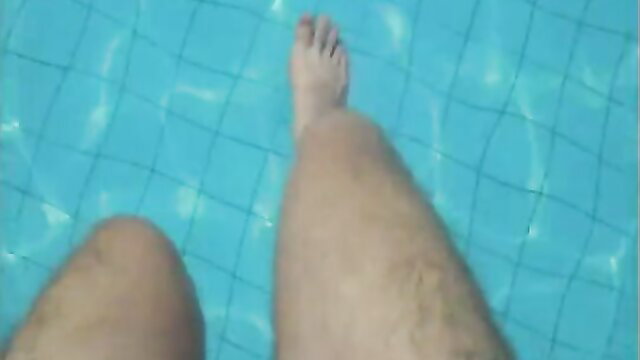 POV view of hairy male legs dipping into turquoise pool water