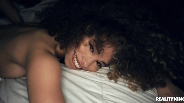 Smiling ebony beauty with curly hair nude on bed in Reality Kings scene
