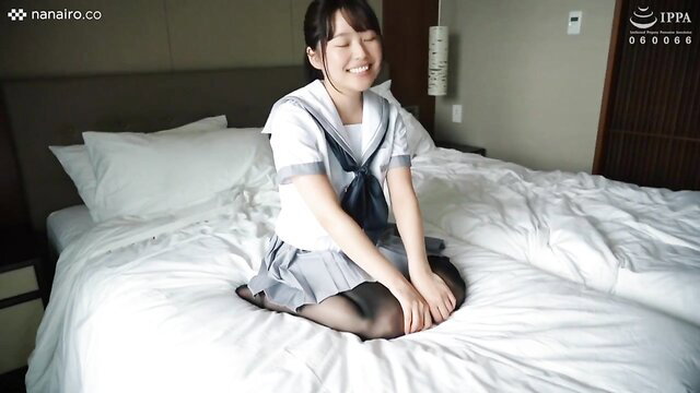 Smiling Asian teen in school uniform sits on bed, stockings upskirt tease