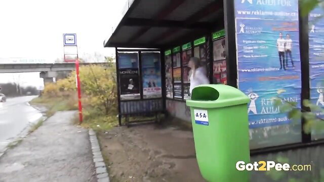 Teen girl pissing in green bin at rainy bus stop outdoors