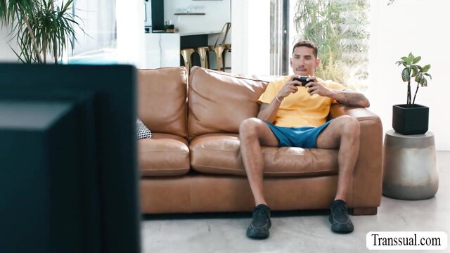Jesse Pony in yellow tank top and blue shorts gaming on couch