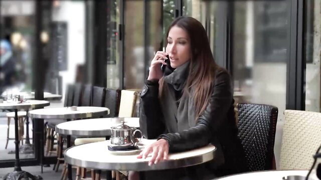 Priva on phone at cafe table in leather jacket and scarf