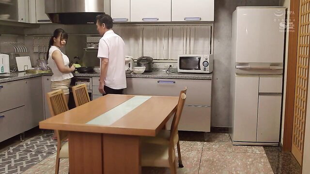 Asian JAV couple in kitchen, woman cooking, man behind her