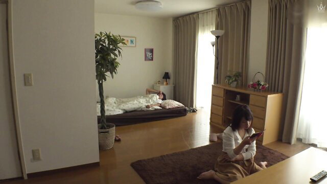 Japanese wife in white blouse skirt sits on tatami, man sleeps nude on futon