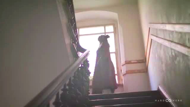 Mystery woman in flowing red dress stands seductively on grand staircase