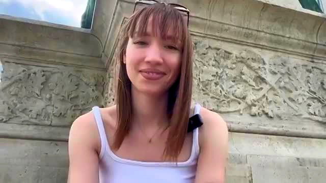 Cute French brunette in white tank top smiles at Paris landmark