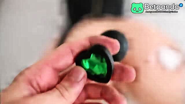 Woman holding black heart butt plug with green gem in bath