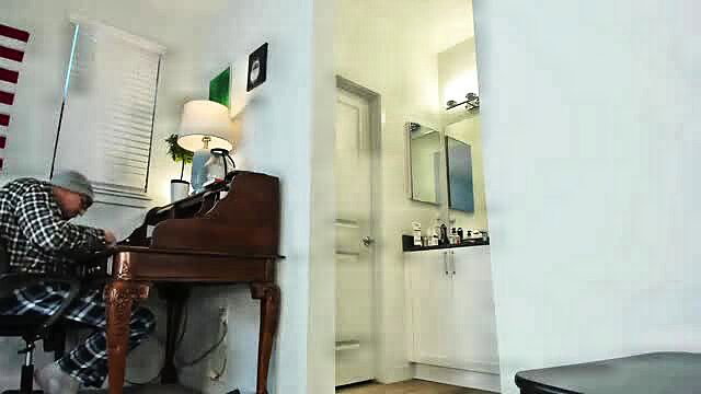 Mature man in plaid shirt and cap sits at desk in adult video thumbnail