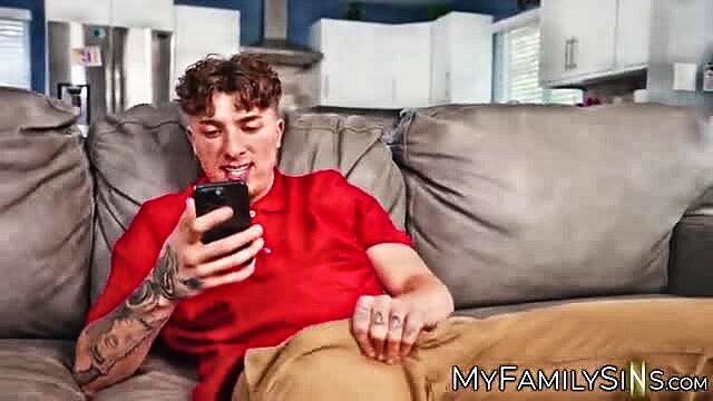 Curly-haired tattooed white guy in red polo and khakis chilling on couch