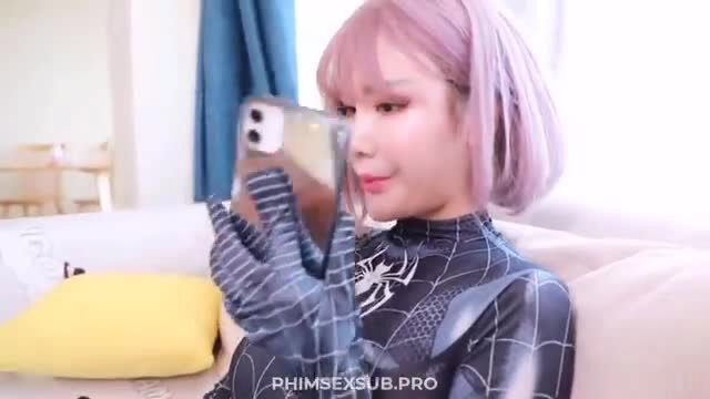 Pink-haired Asian girl in sexy Spiderman cosplay holds phone selfie