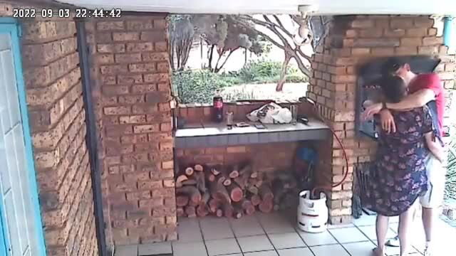 Cheating wife in floral dress hugs man passionately on patio CCTV