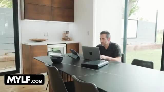 Cory Chase working at desk next to oblivious husband in steamy scene