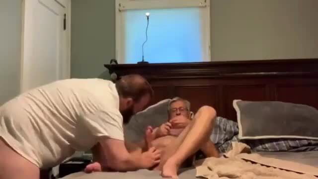 Bald muscular guy groping nude elderly man's crotch on bed