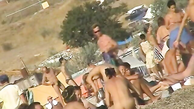 Crowded nude beach with many naked men sunbathing and chatting